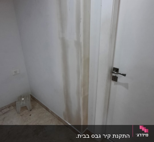 קיר גבס עם סימני רטיבות ליד דלת לבנה